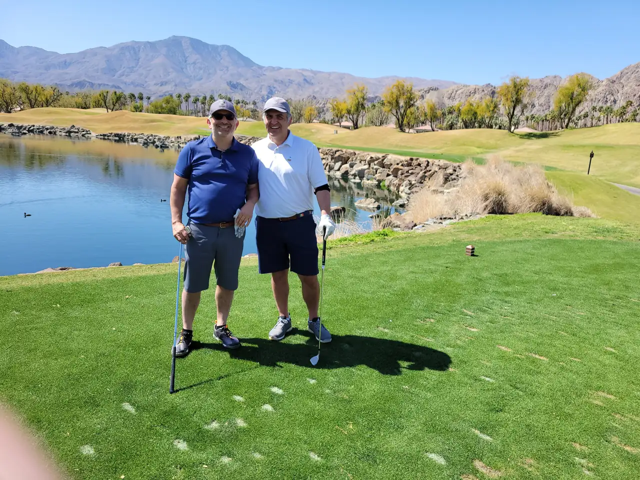 The Perry Bros on a lakeside tee at the PGA West Stadium Course, mountains behind them